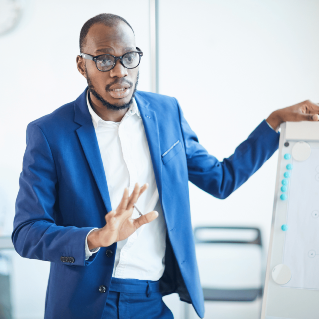 A man stands at the front of the room leading an employee coaching session