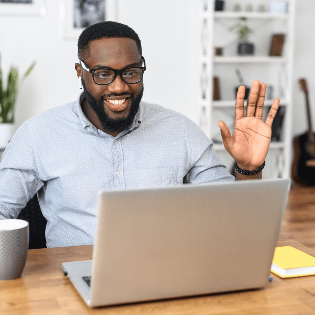 A man waves to someone on his laptop screen as he starts his employee coaching session