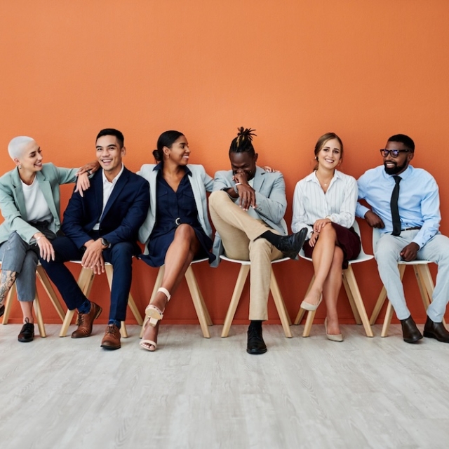 A group of people sitting in front of an orange background, smiling as they discuss the benefits of Sanctus Coaching